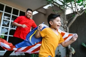 happy malaysian kid run around the house carrying malaysia flag